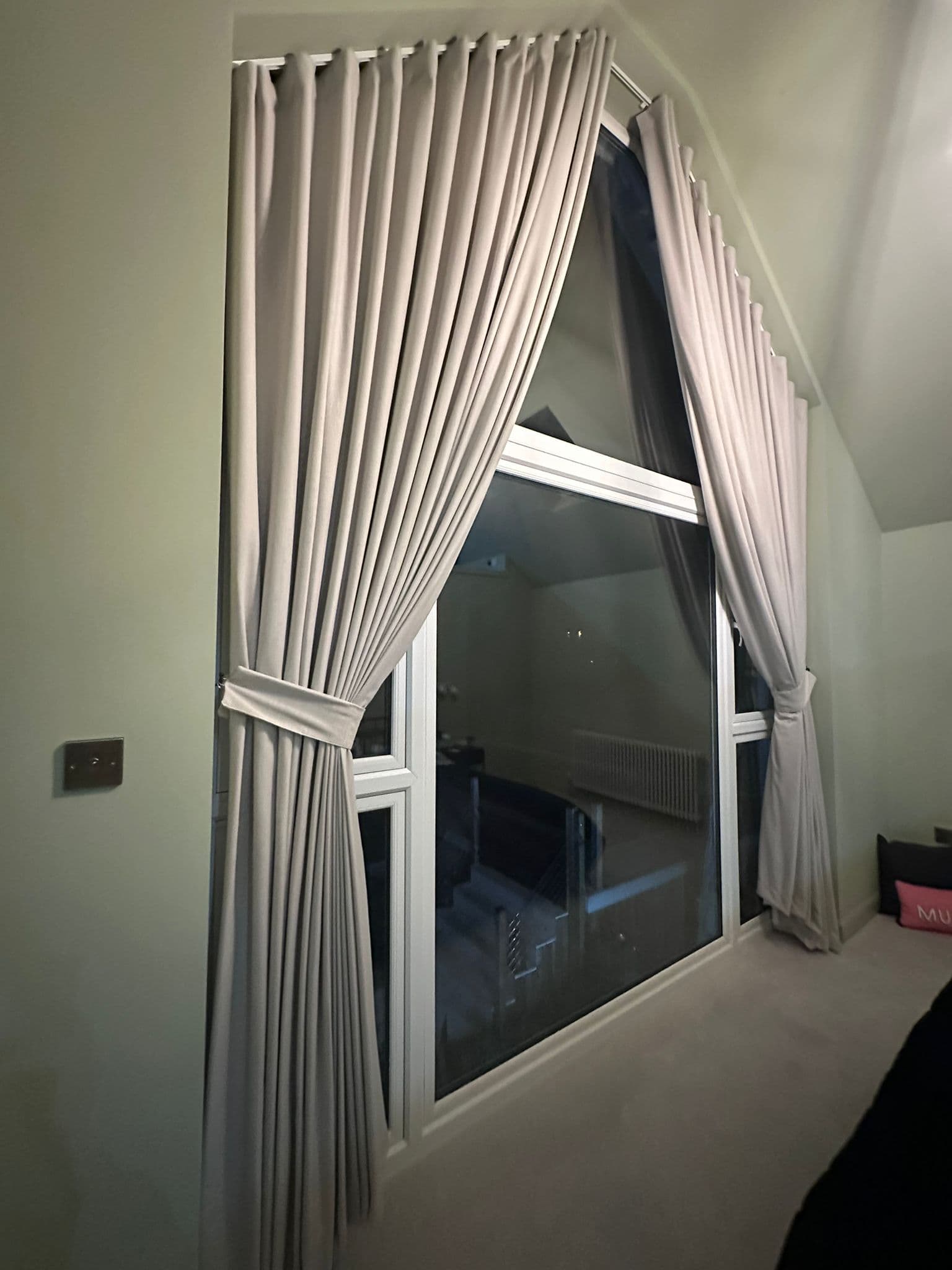 Soft ivory curtains following an angled ceiling, gathered to frame tall glazing