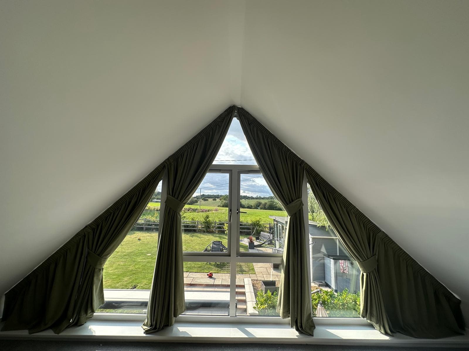 Olive green curtains gathered into matching fabric tiebacks around a triangular window